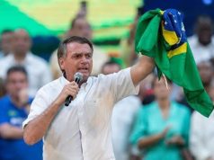 Jair Bolsonaro de camisa branca e segurando bandeira do Brasil