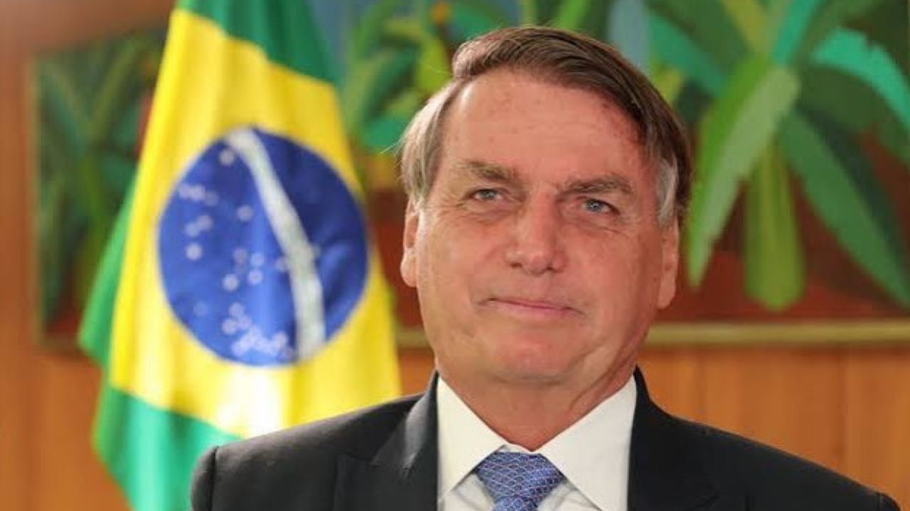 Jair Bolsonaro de terno e gravata olhando pra frente com expressão de ironia