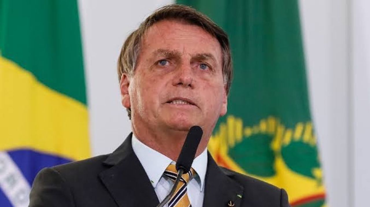 Jair Bolsonaro de terno e gravata, falando em microfone com expressão séria