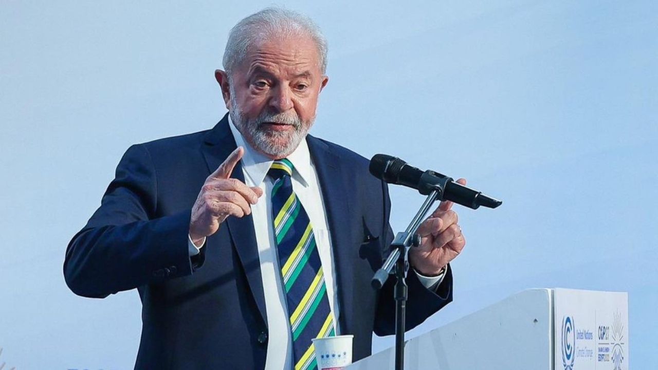 Luiz Inácio Lula da Silva falando em microfone e gesticulando, de terno e gravata