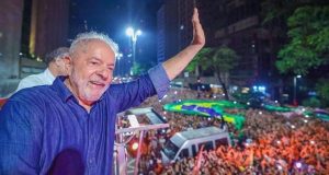 Lula de camisa jeans sorrindo e acenando para o povo em cima de carro de som