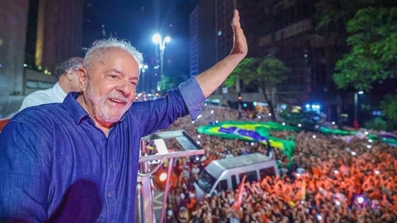Lula de camisa jeans sorrindo e acenando para o povo em cima de carro de som