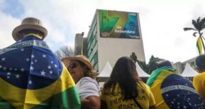 Bolsonaristas com roupas verdes e amarelas perto de outdoor de 7 de setembro