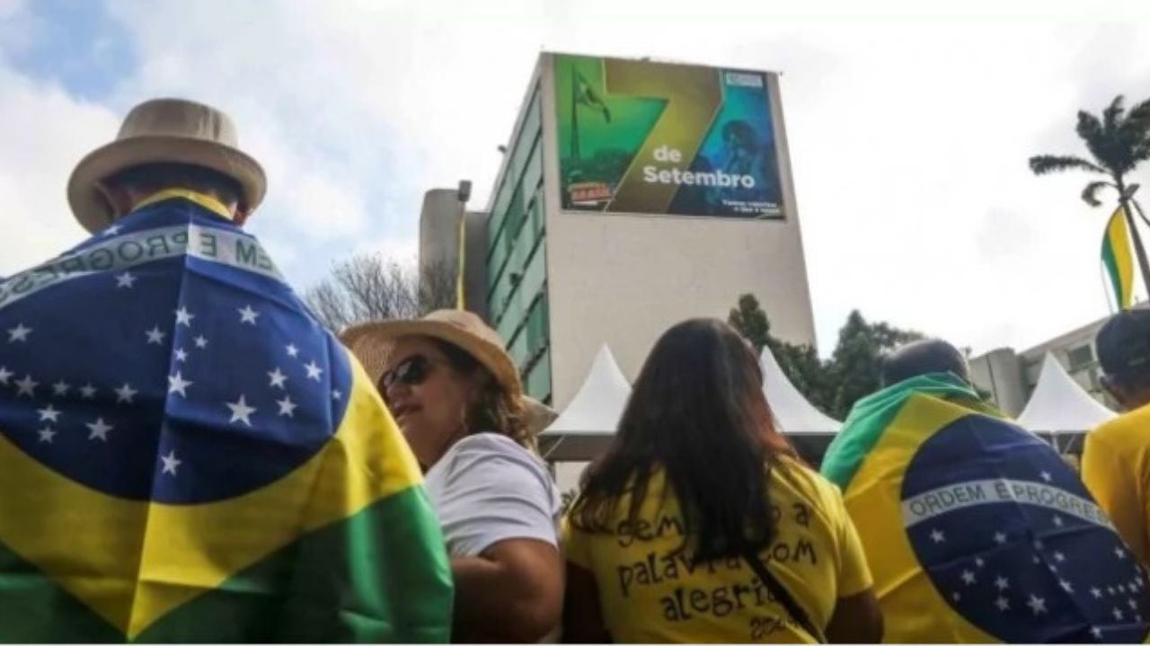 Bolsonaristas com roupas verdes e amarelas perto de outdoor de 7 de setembro