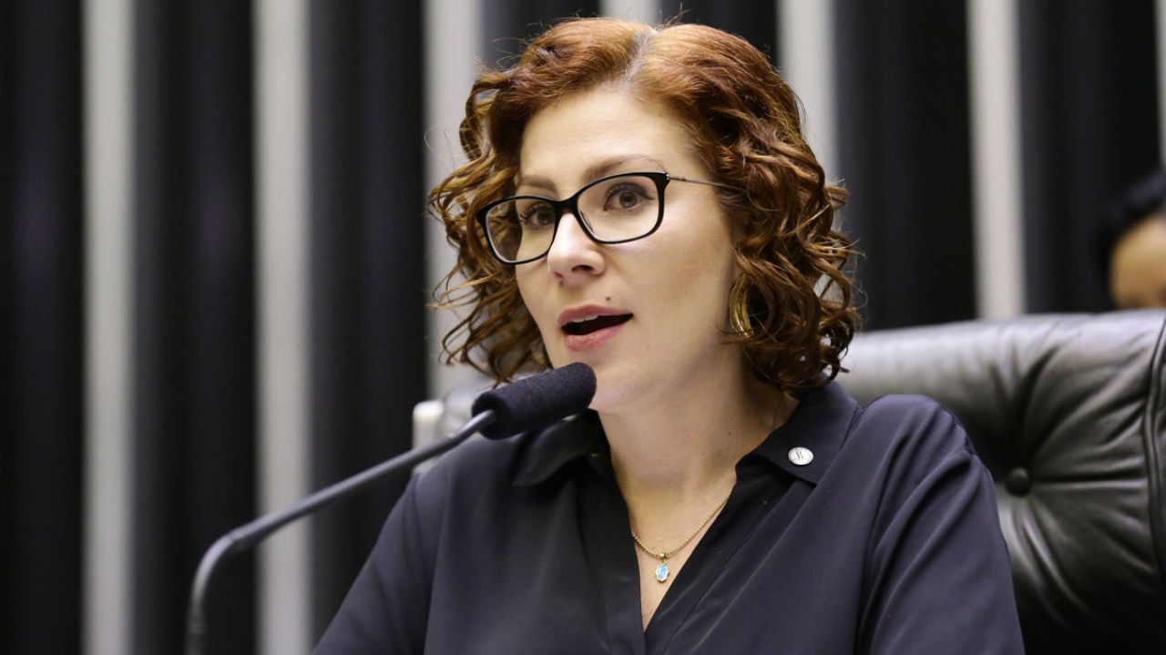Carla Zambelli de roupa preta e óculos, falando em microfone