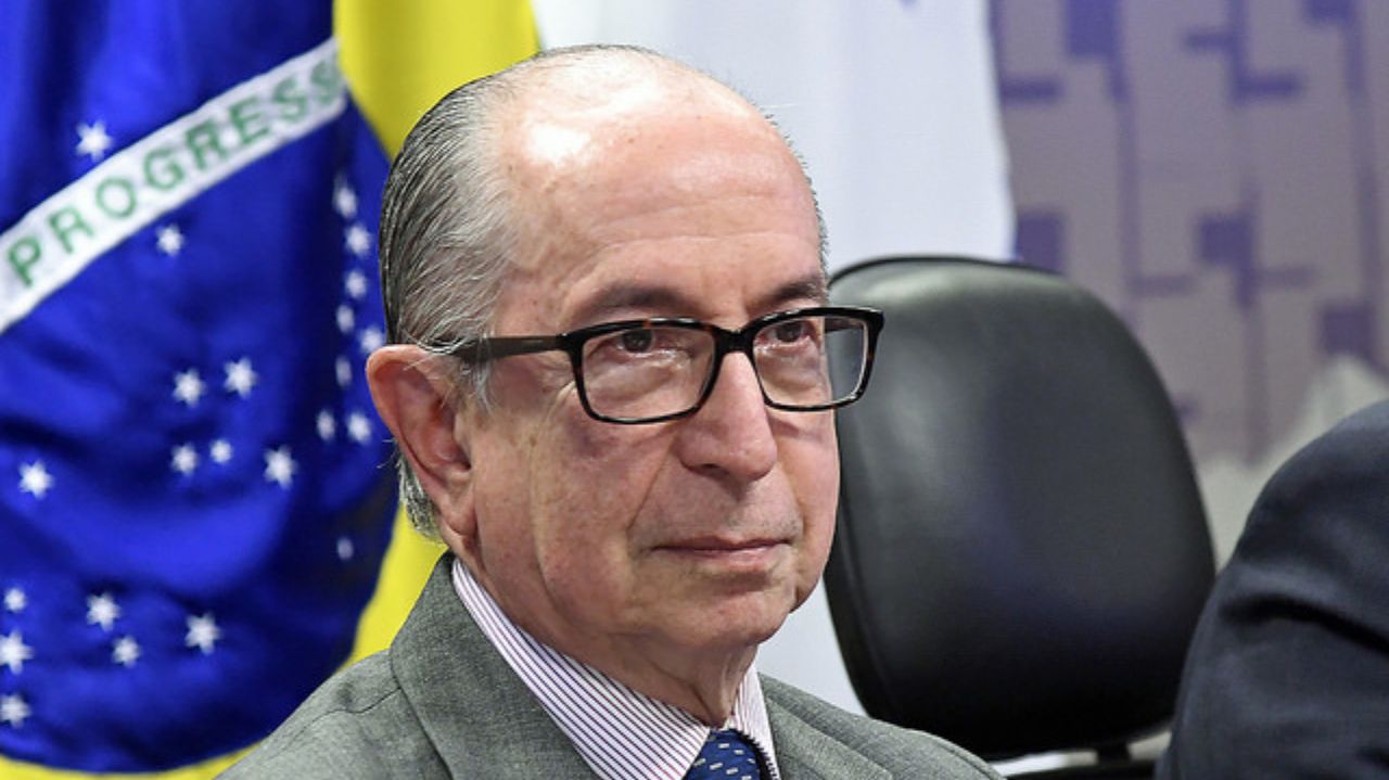 Marcos Cintra de óculos e expressão séria, perto de bandeira do Brasil
