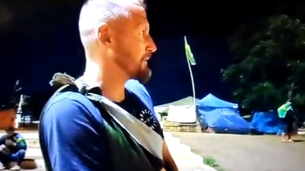 Bolsonarista de lado, com camiseta azul marinho e bandeira do brasil amarrada ao corpo