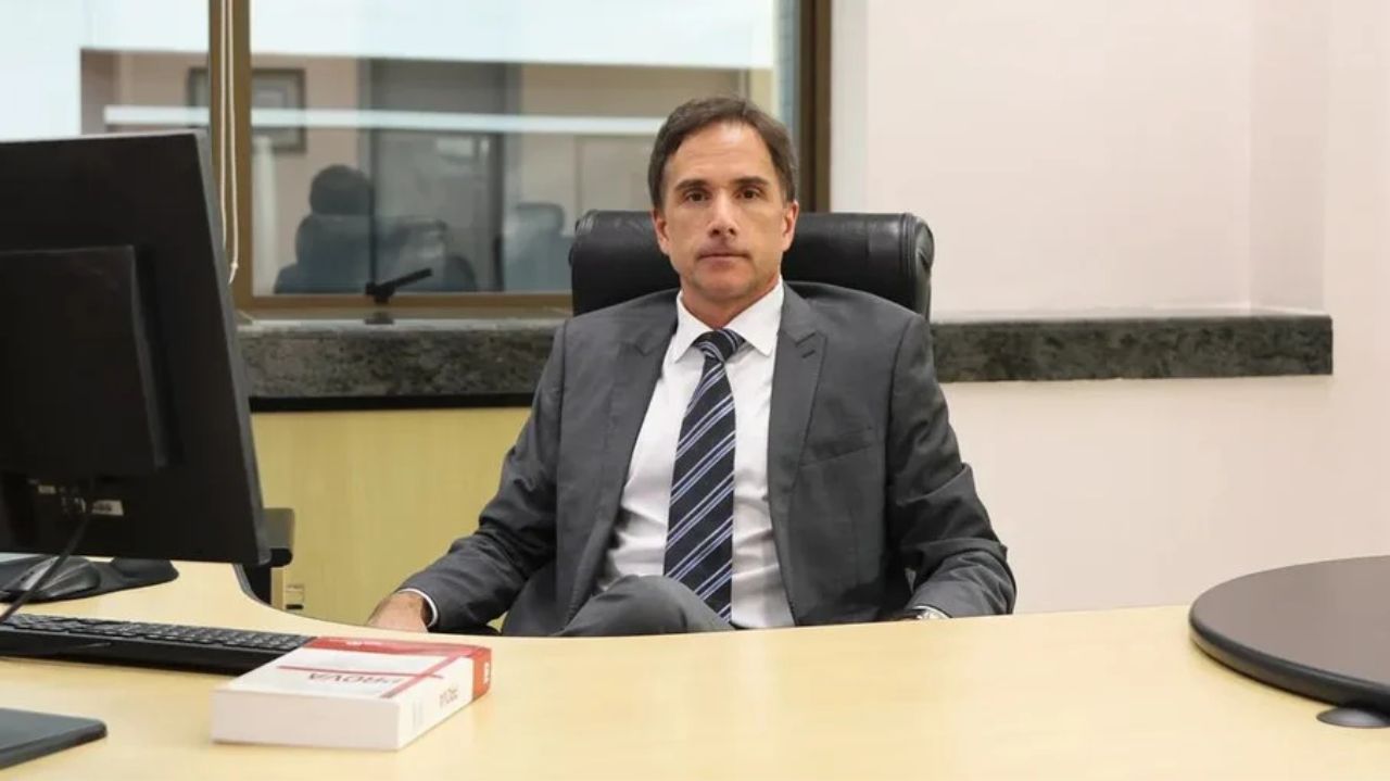 Eduardo Fernando Appio de terno e gravata, sentado e posando para foto perto de mesa de escritório
