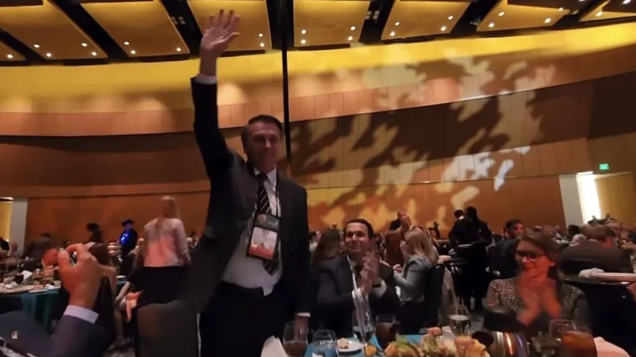 Jair Bolsonaro com o braço erguido e sorrindo em evento
