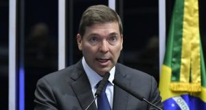 Josué Gomes Silva de terno e gravata, falando em microfone com expressão assustada