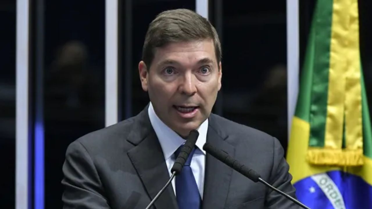 Josué Gomes Silva de terno e gravata, falando em microfone com expressão assustada