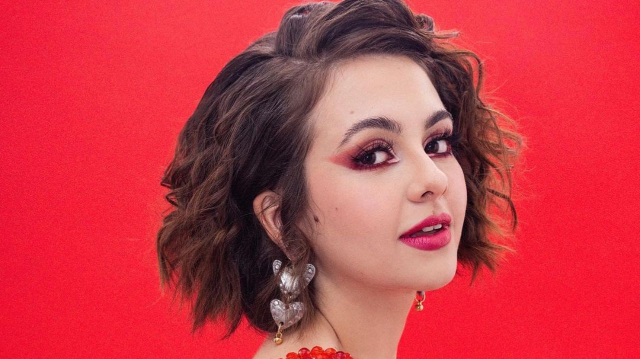 Klara Castanho de perfil, em fundo vermelho, com brincos grandes