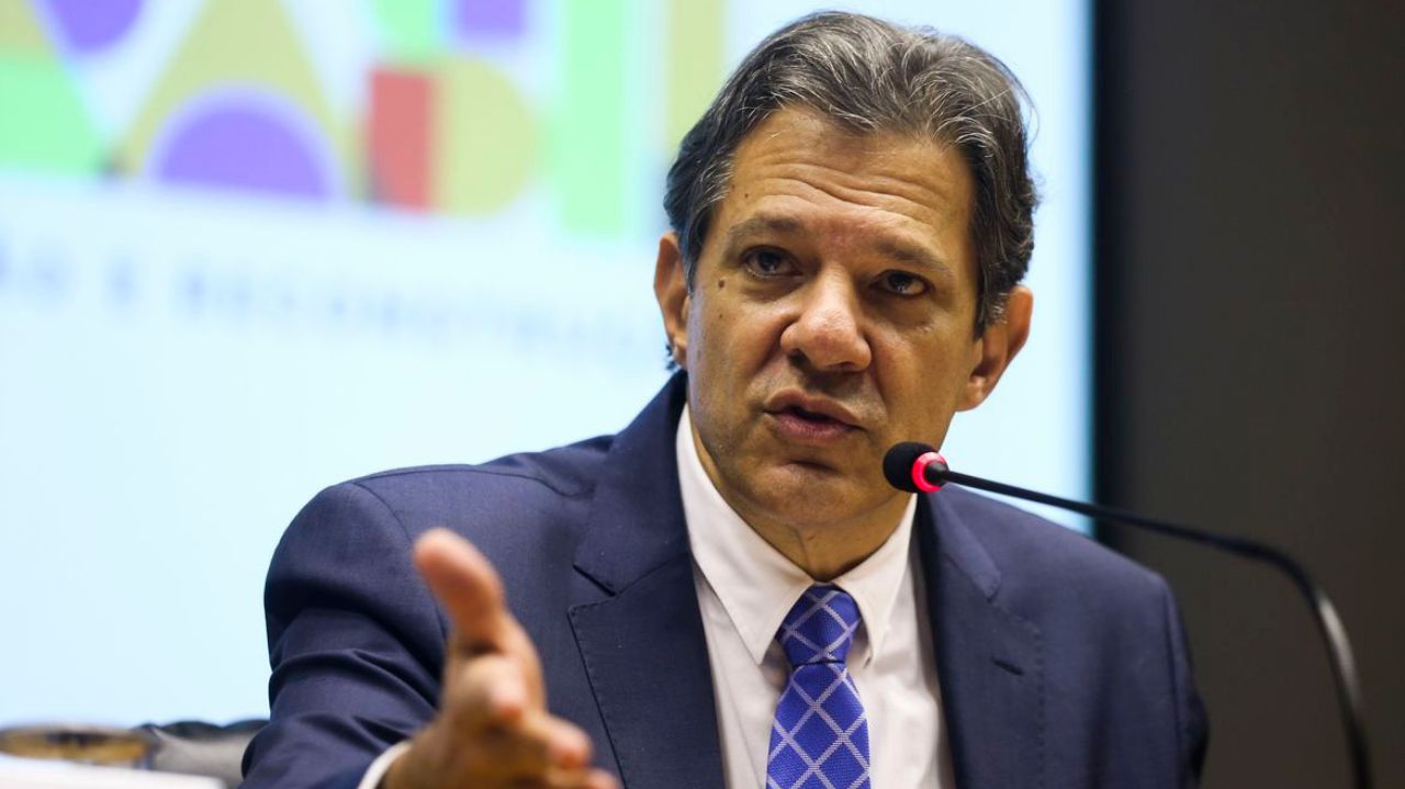 Fernando Haddad de terno e gravata azuis e camisa branca, falando e gesticulando