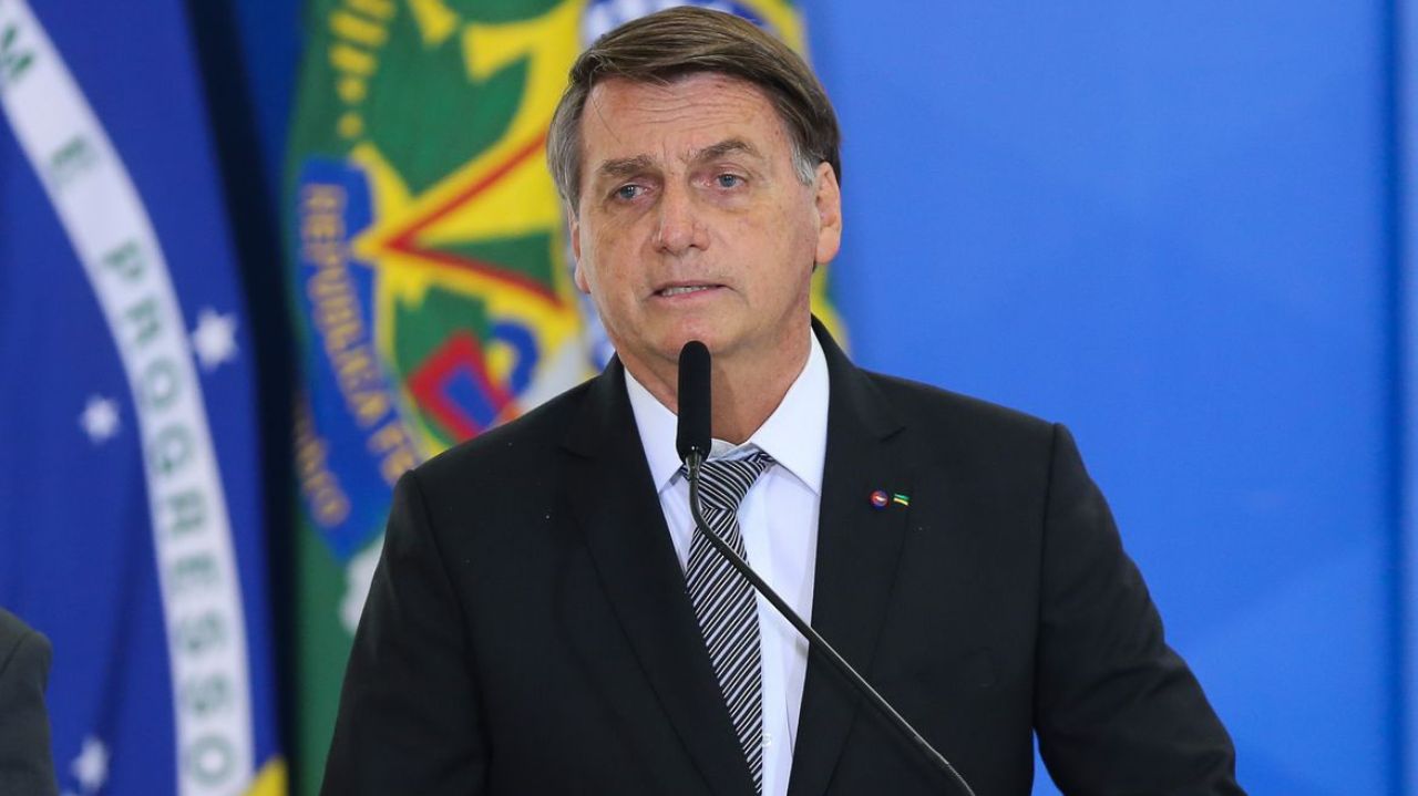 Jair Bolsonaro de terno e gravata, falando em microfone
