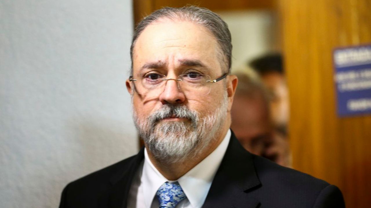 Augusto Aras olhando pra frente, com expressão séria, de óculos