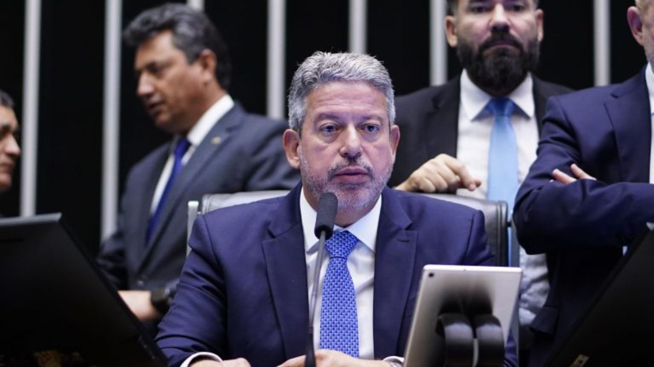 Arthur Lira falando em microfone cercado de parlamentares