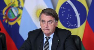 Jair Bolsonaro com expressão séria perto de bandeiras de países