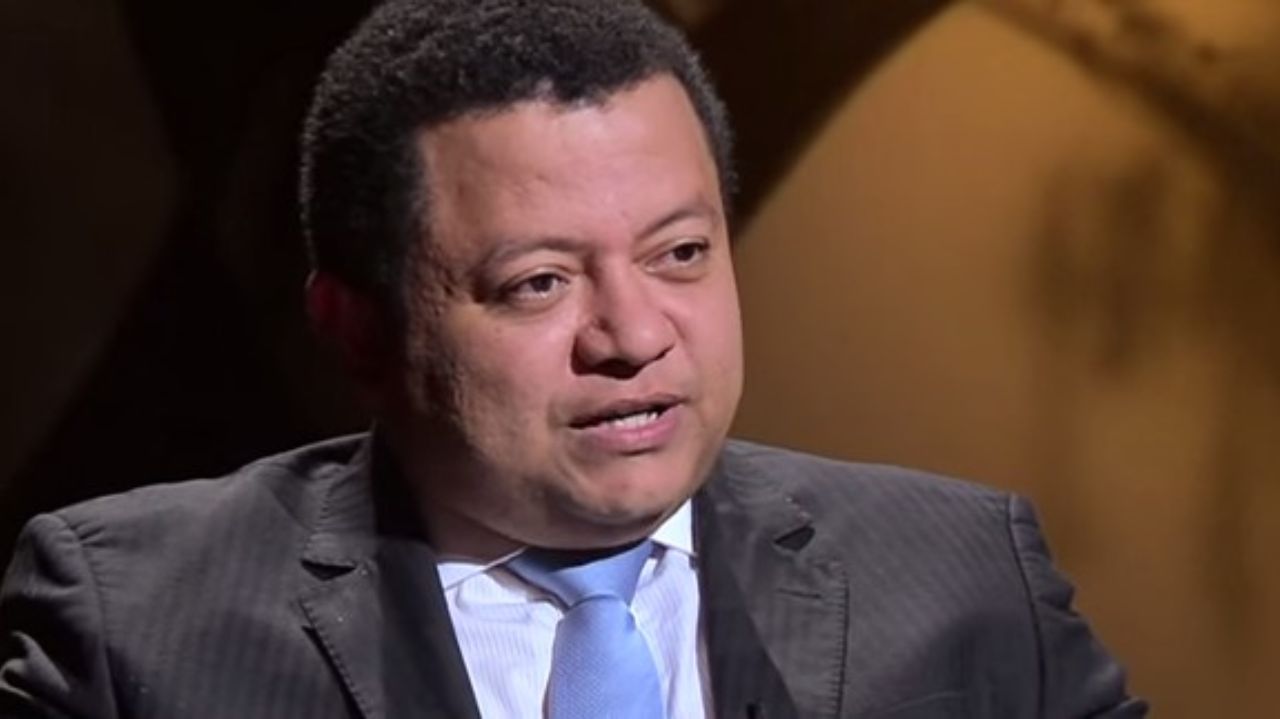 Márlon Reis de terno escuro e gravata azul, falando