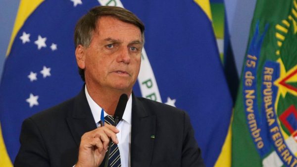 Jair Bolsonaro de terno e gravata, com expressão pensativa, falando em microfone