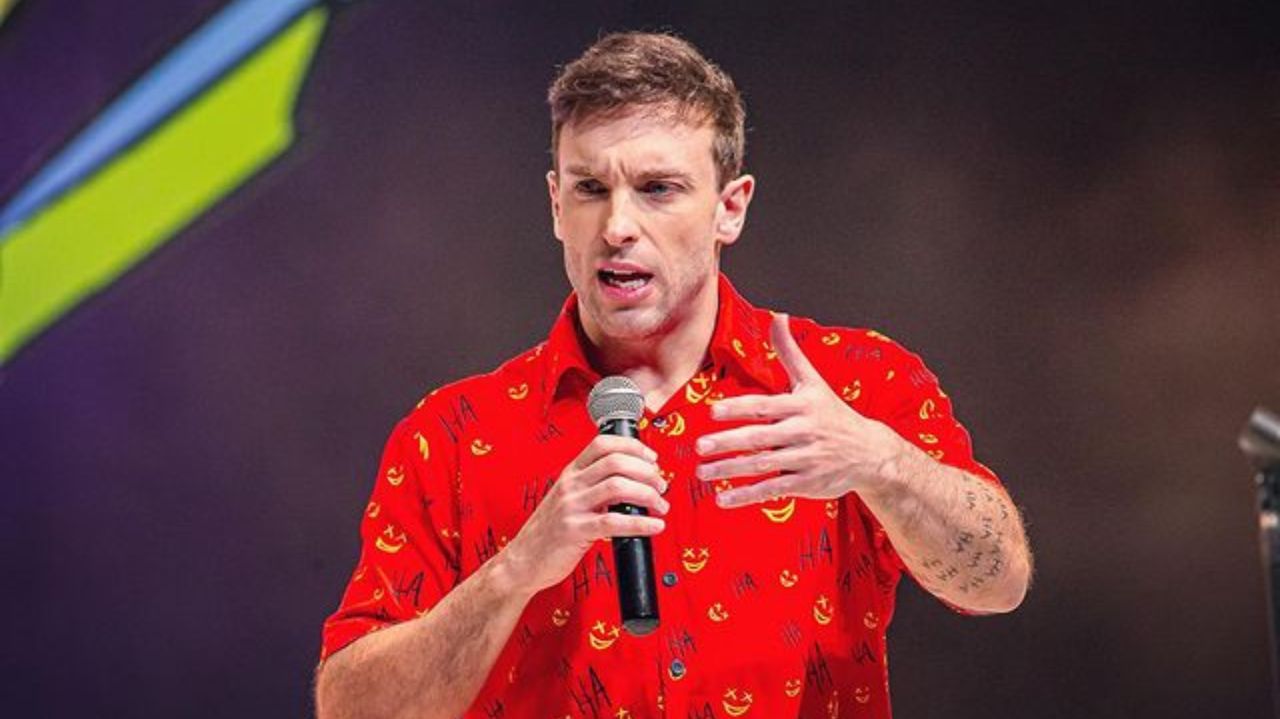 Léo Lins de camisa vermelha, falando e gesticulando, com microfone