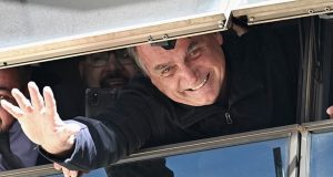 Jair Bolsonaro sorrindo e acenando pela janela