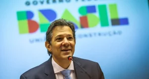 Fernando Haddad olhando pra frente e sorrindo, perto de microfone, com roupa social