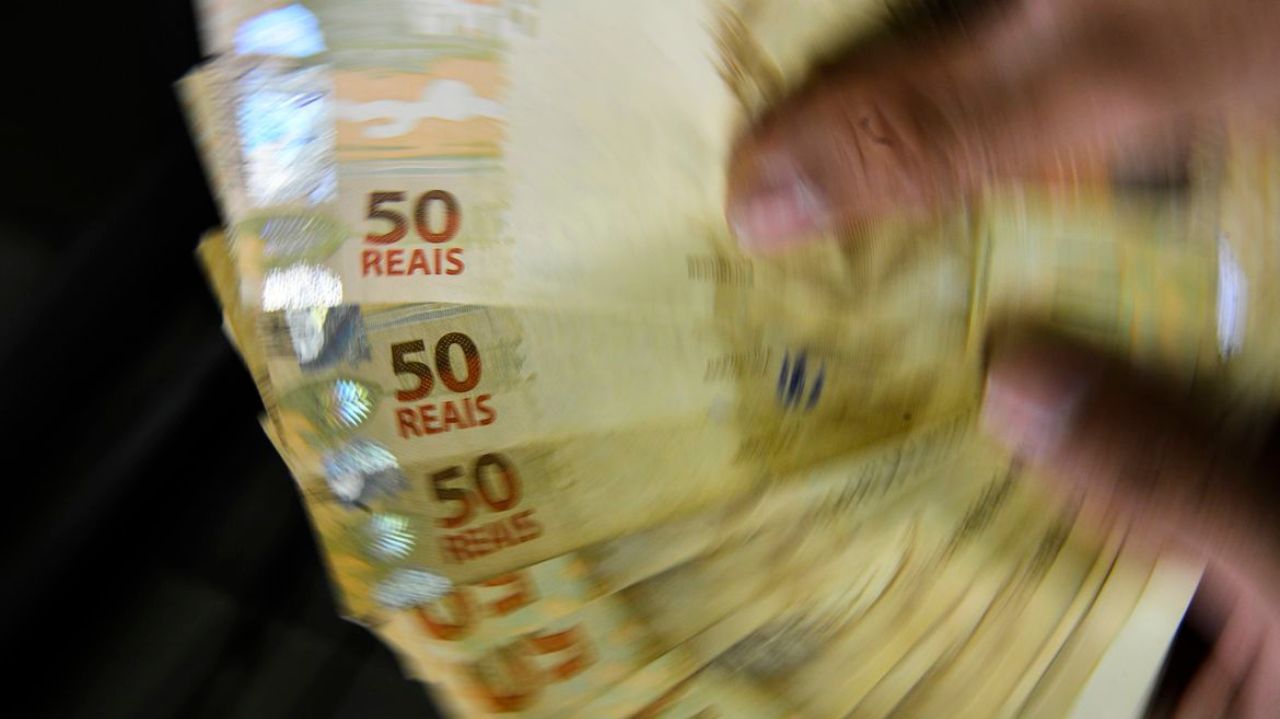 Mãos contando notas de 50 reais