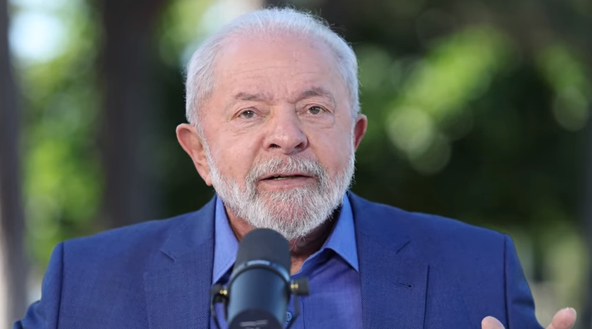 Lula de roupa social azul, falando em microfone e olhando pra câmera