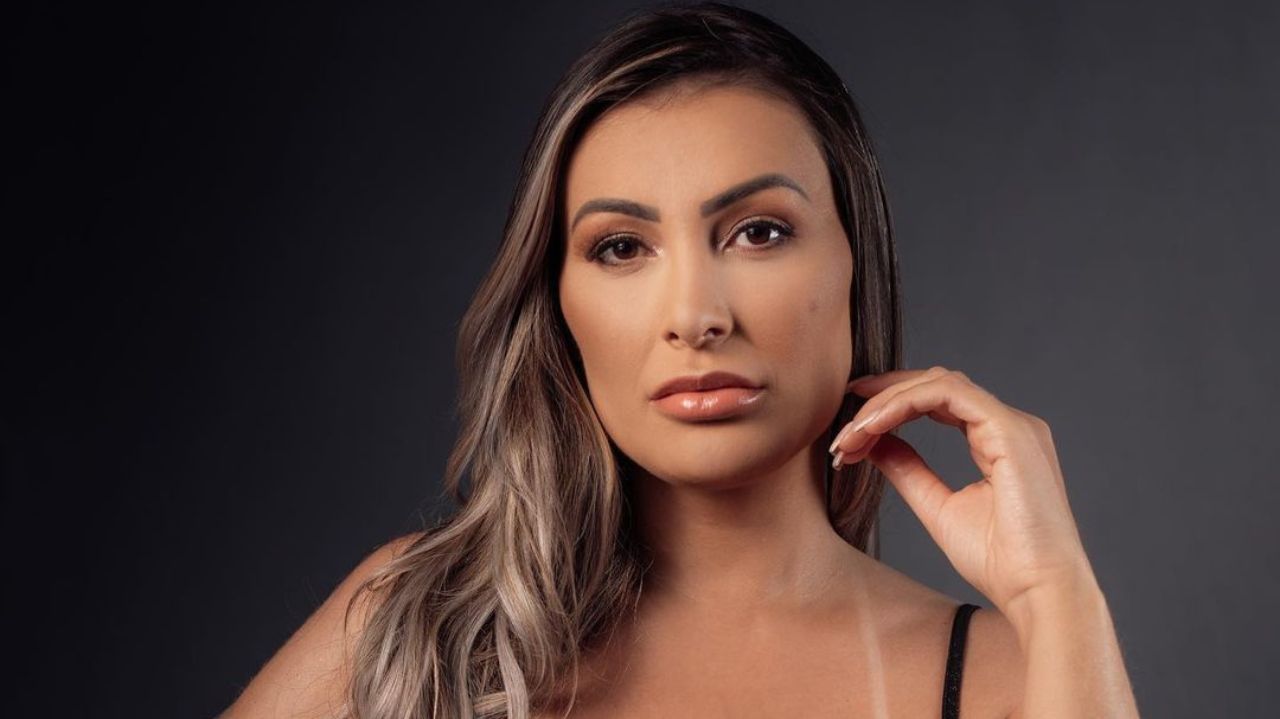 Andressa Urach fazendo carão, com mão próxima ao queixo e cabelo solto