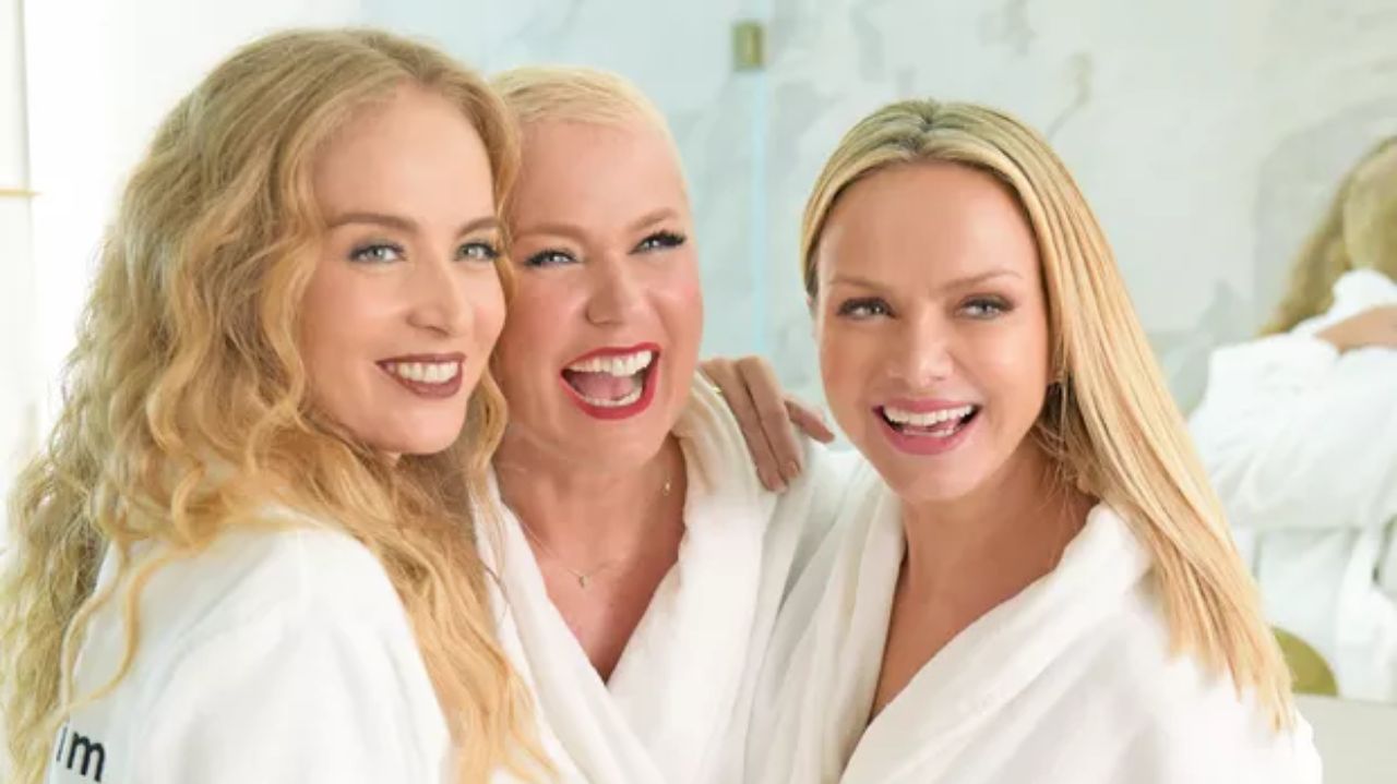 Angélica, Xuxa e Eliana sorrindo, abraçadas, de roupões brancos