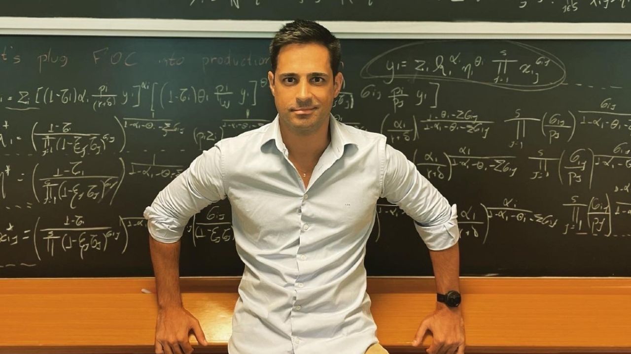 Leo Siqueira de camisa social clara, apoiado em quadro negro com números