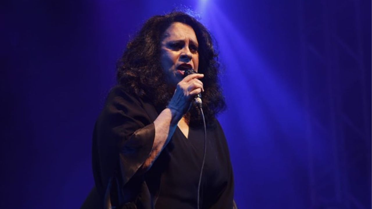 Gal Costa cantando em microfone, de roupa preta