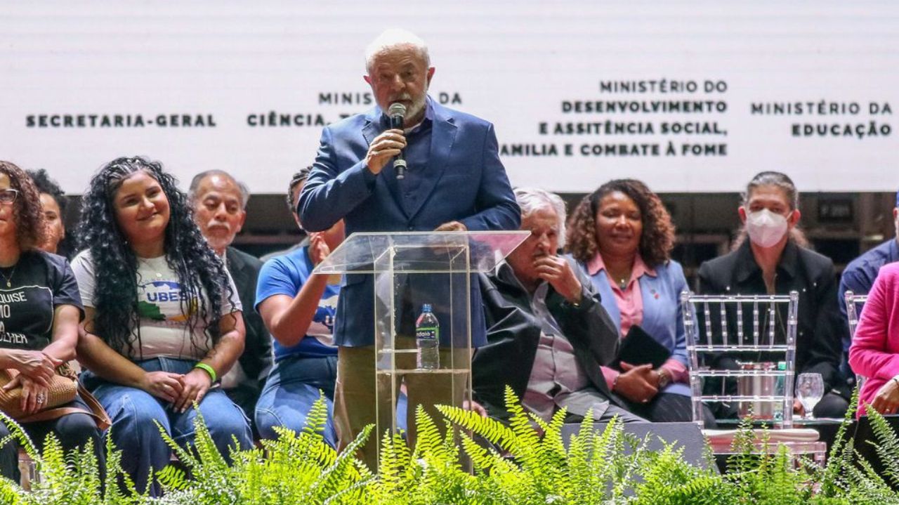 Lula discursando com microfone na mão e roupa social azul