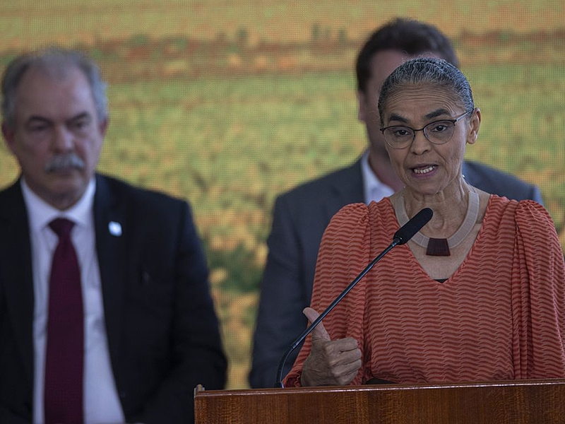 Marina Silva de roupa vermelha e cabelo preso, falando em microfone e gesticulando