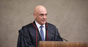 Alexandre de Moraes olhando para o lado e sorrindo, perto de microfone