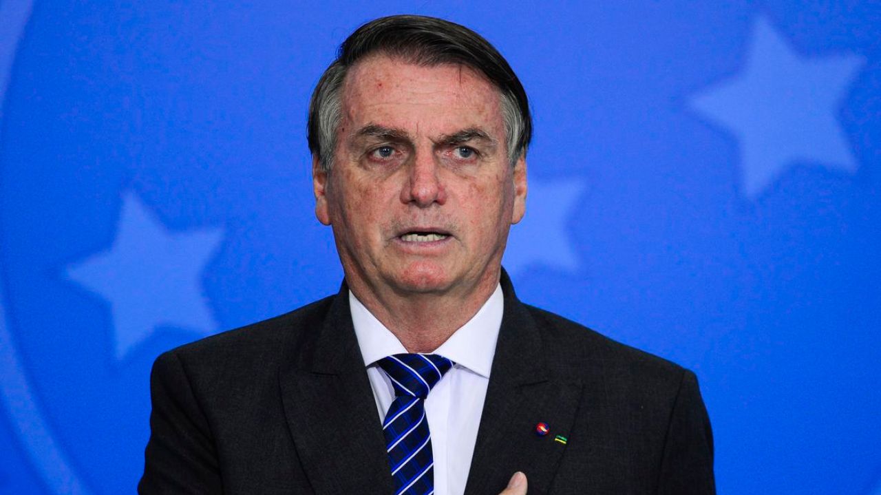 Jair Bolsonaro com roupa social, expressão séria e com fundo azul