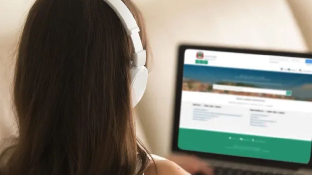Menina de costas olhando para a tela do notebook, com fones de ouvido brancos