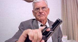 Erasmo Dias com expressão séria, segurando arma