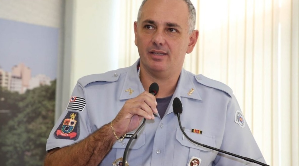 Aleksander Lacerda fardado olhando para o lado e segurando microfone
