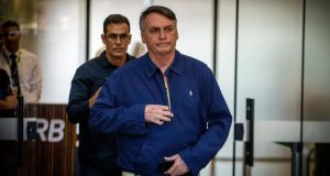 Bolsonaro de roupa de frio azul, andando com expressão séria