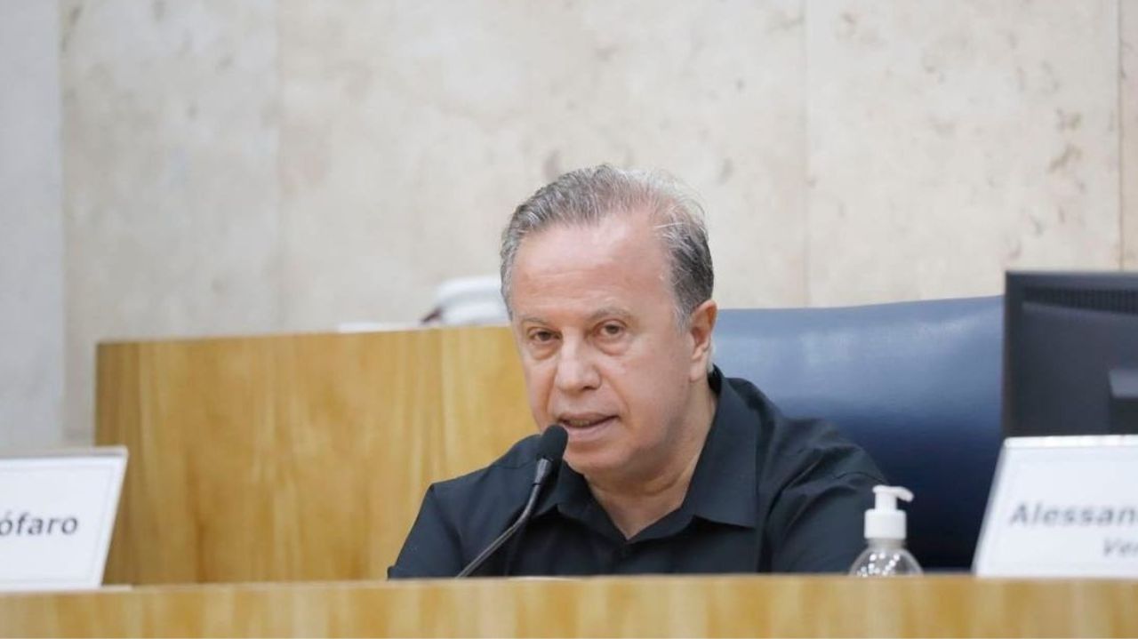 Vereador Camilo Cristófaro falando em microfone com expressão séria e olhando para o lado