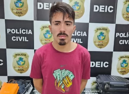 José Henrique Aguiar Soares de camiseta roxa em delegacia, com expressão séria