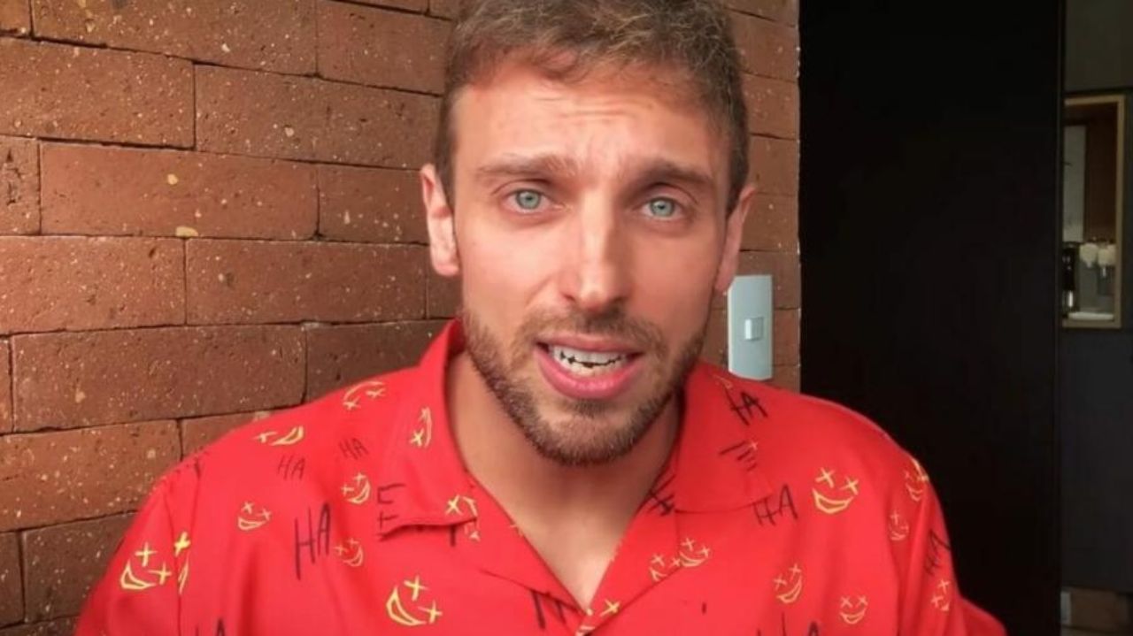 Léo Lins de camisa vermelha estampada, falando com expressão de preocupação
