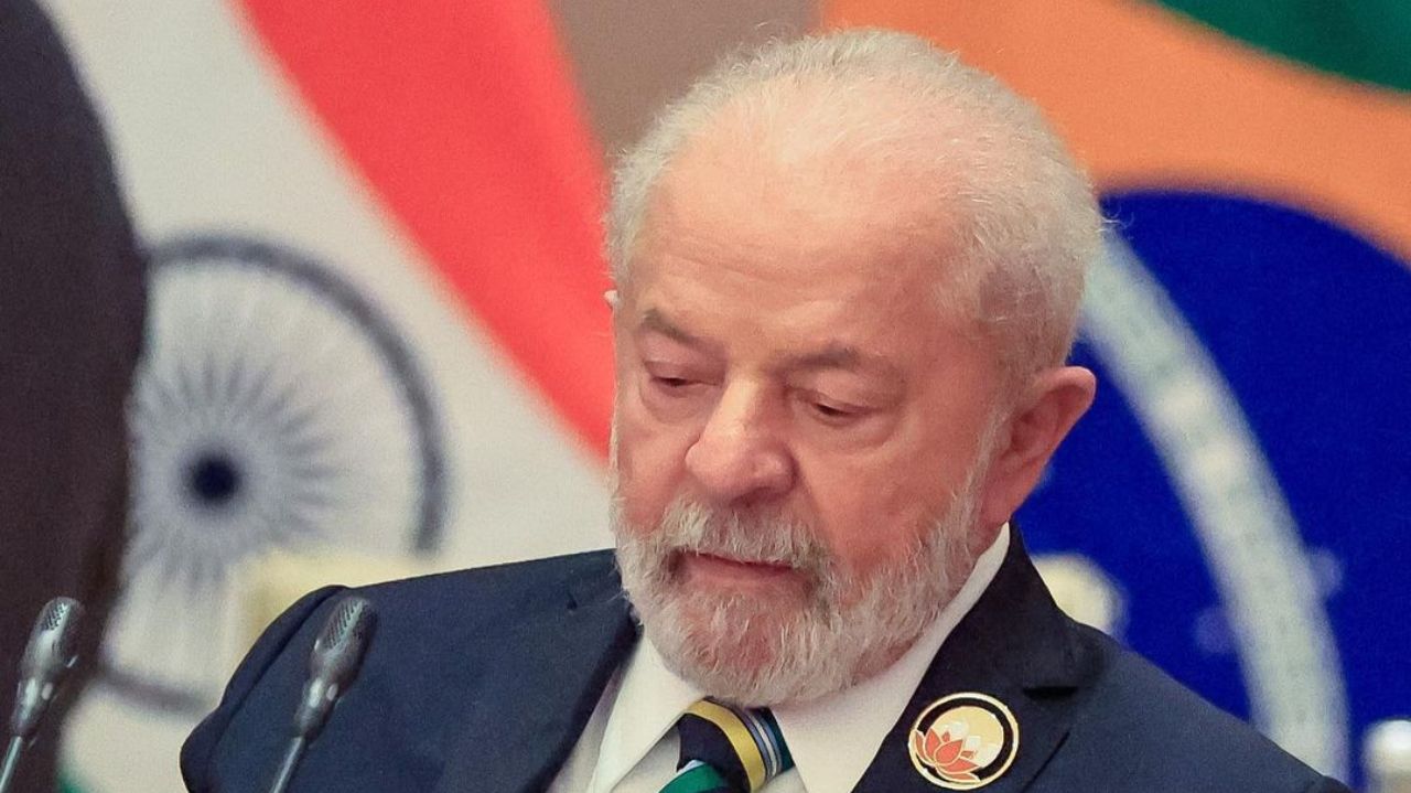 Lula olhando pra baixo com bandeiras ao fundo