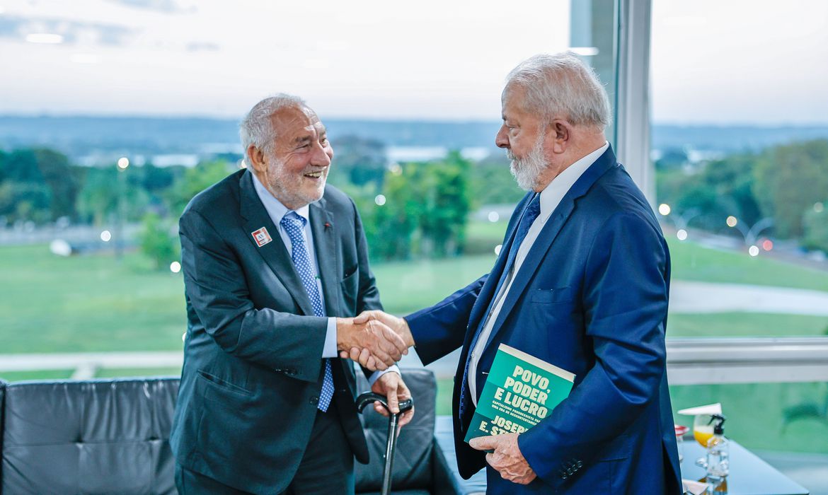 Lula e Stiglitz em aperto de mãos, os dois sorrindo e com trajes formais
