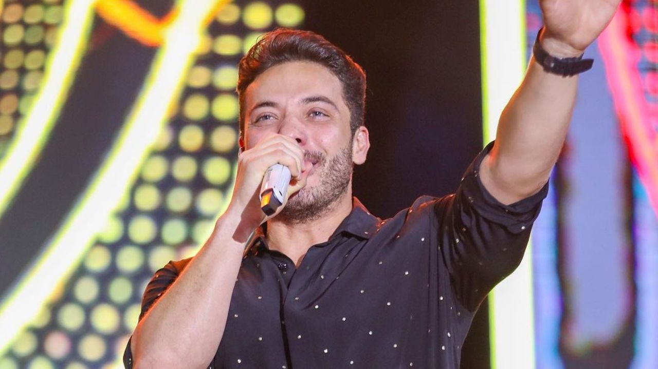 Wesley Safadão segurando microfone e com braço levantado em show
