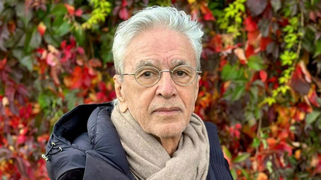Caetano Veloso posando perto de parede florida, com expressão séria
