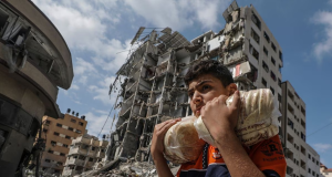 Jovem palestino carregando sacos de pão em meio a escombros em Gaza