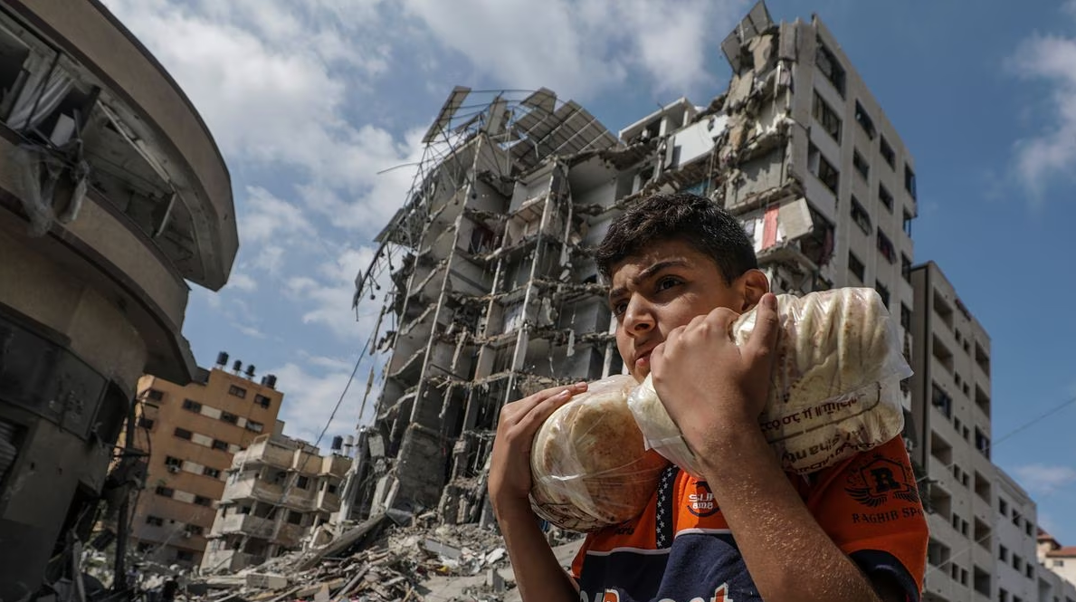 Jovem palestino carregando sacos de pão em meio a escombros em Gaza