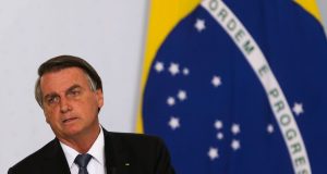 Jair Bolsonaro com bandeira do Brasil ao fundo e expressão de preocupação